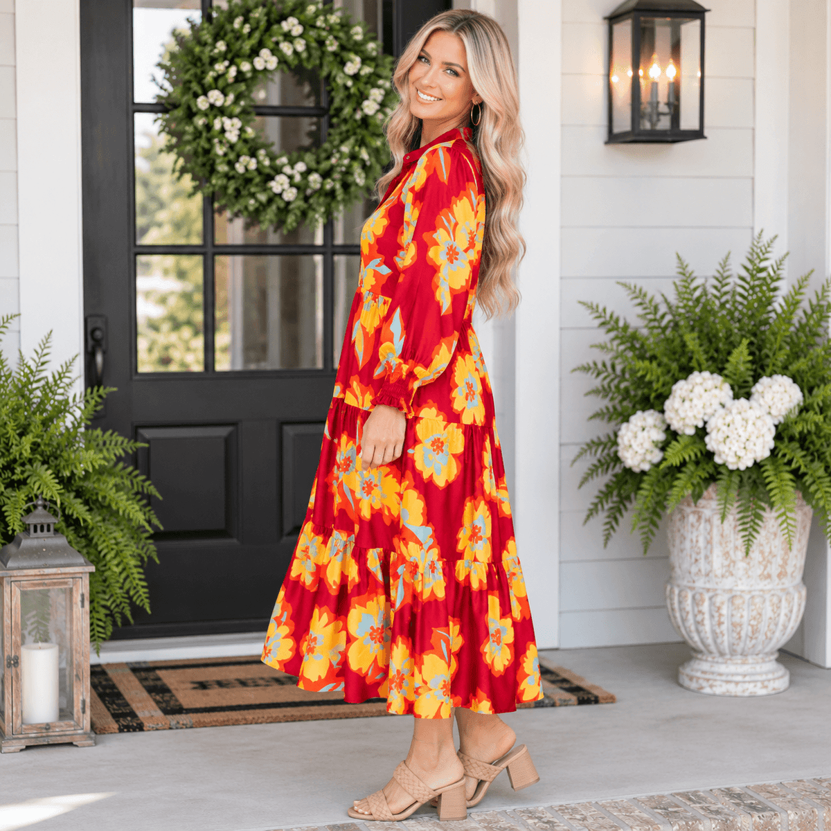 Model wearing a vibrant SOUL FIRE DRESS with floral patterns, standing by a decorative front porch.