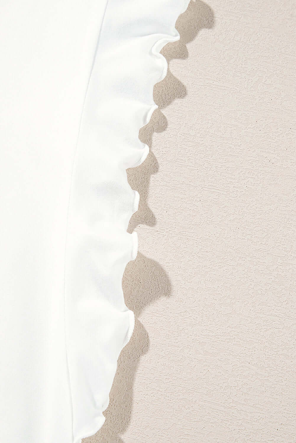 Close-up of the ruffled edge of a white tank top, showcasing soft fabric and delicate design details.