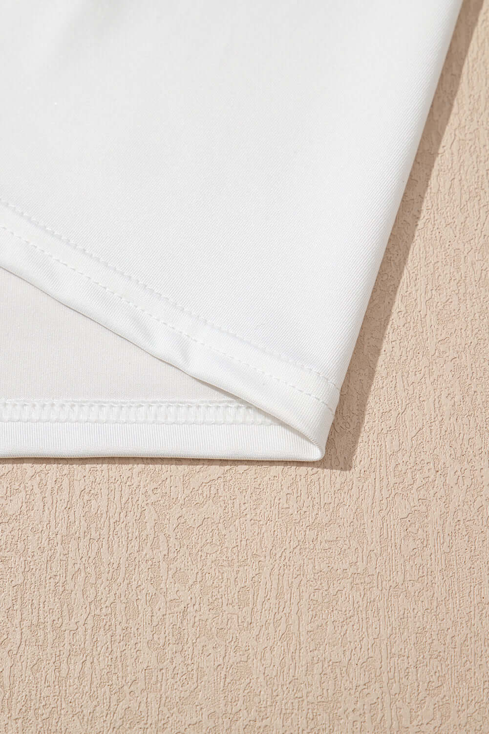 Close-up of the hem detail of a white fabric, showcasing a smooth finish and stitching.