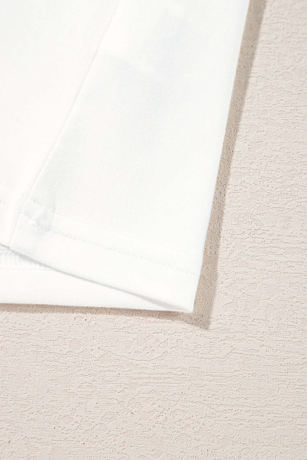 Close-up of the hem and fabric texture of a soft white shirt on a light textured background.