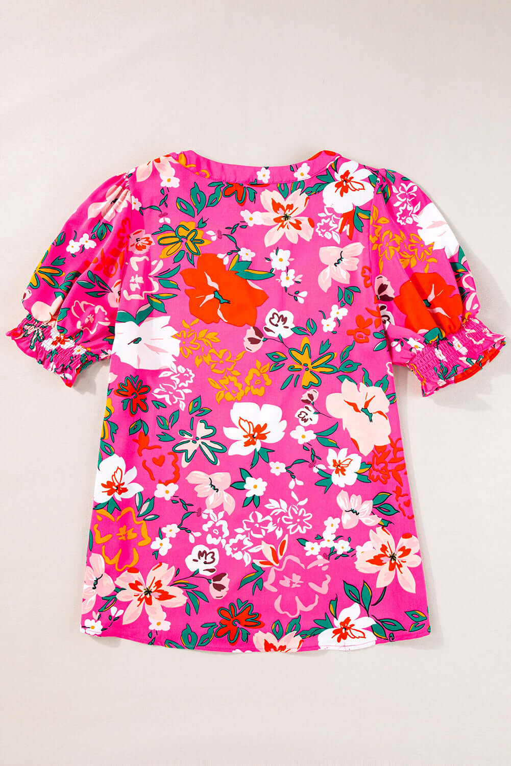 Paradise Petals top: vibrant floral print blouse with puff sleeves and split V-neckline on pink background.