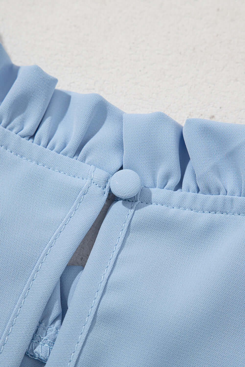 Close-up of Frill Seeker Top in sky blue, featuring delicate ruffle trim and button detail.