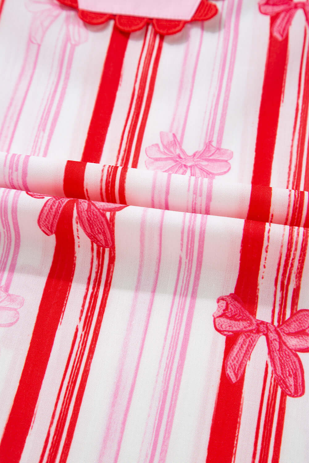 Close-up of striped fabric with pink and red bow prints for Ribbon Reign Top, showcasing a playful and feminine design.