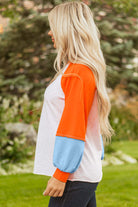 Woman wearing CITRUS CRUSH TOP with orange sleeves and blue cuffs, showcasing a vibrant color block design.