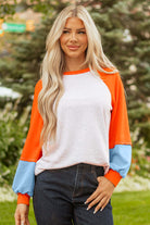 Model wearing CITRUS CRUSH TOP featuring color block design with orange sleeves, blue cuffs, and grey body in outdoor setting.