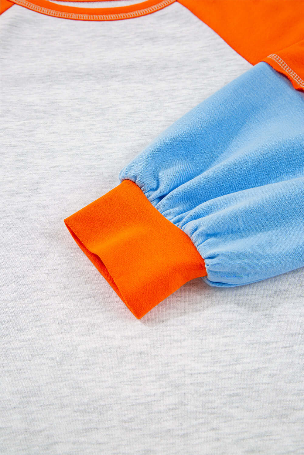 Close-up of CITRUS CRUSH TOP showcasing the vibrant tangerine sleeve and soft sky blue cuff against a light grey body.