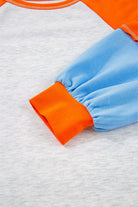 Close-up of CITRUS CRUSH TOP showcasing the vibrant tangerine sleeve and soft sky blue cuff against a light grey body.