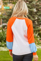 Back view of the CITRUS CRUSH TOP showcasing vibrant tangerine sleeves, light grey body, and soft sky blue cuffs.