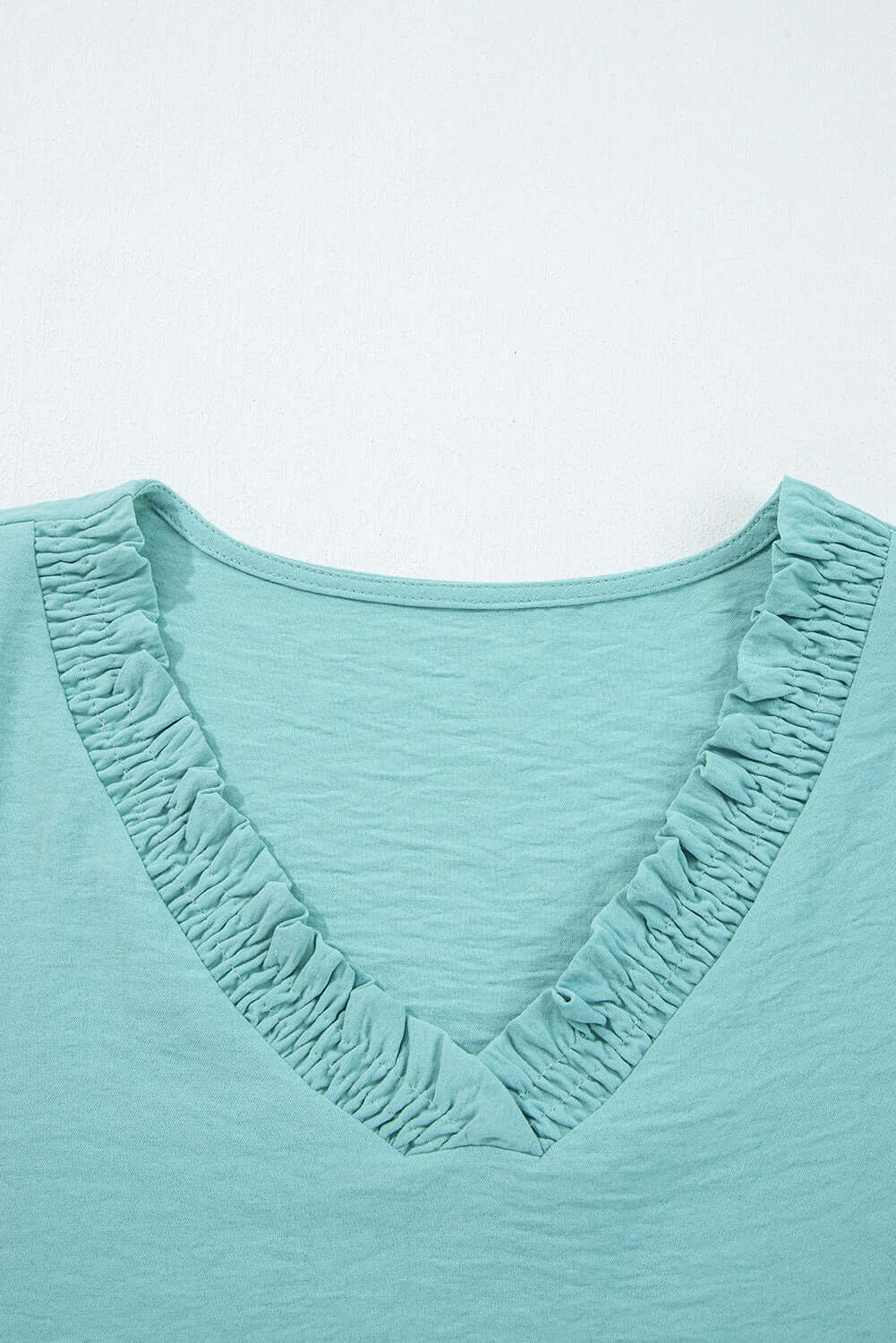 Close-up of the frilled V-neckline on the GRACEFUL GLOW TOP (jade sea), showcasing its elegant design and texture.