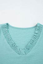 Close-up of the frilled V-neckline on the GRACEFUL GLOW TOP (jade sea), showcasing its elegant design and texture.