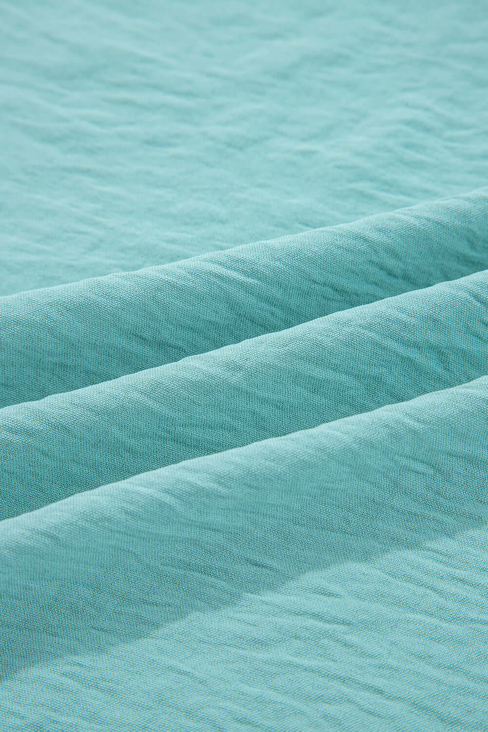 Close-up of crinkled fabric texture in jade sea, showcasing the material of the GRACEFUL GLOW TOP (jade sea).