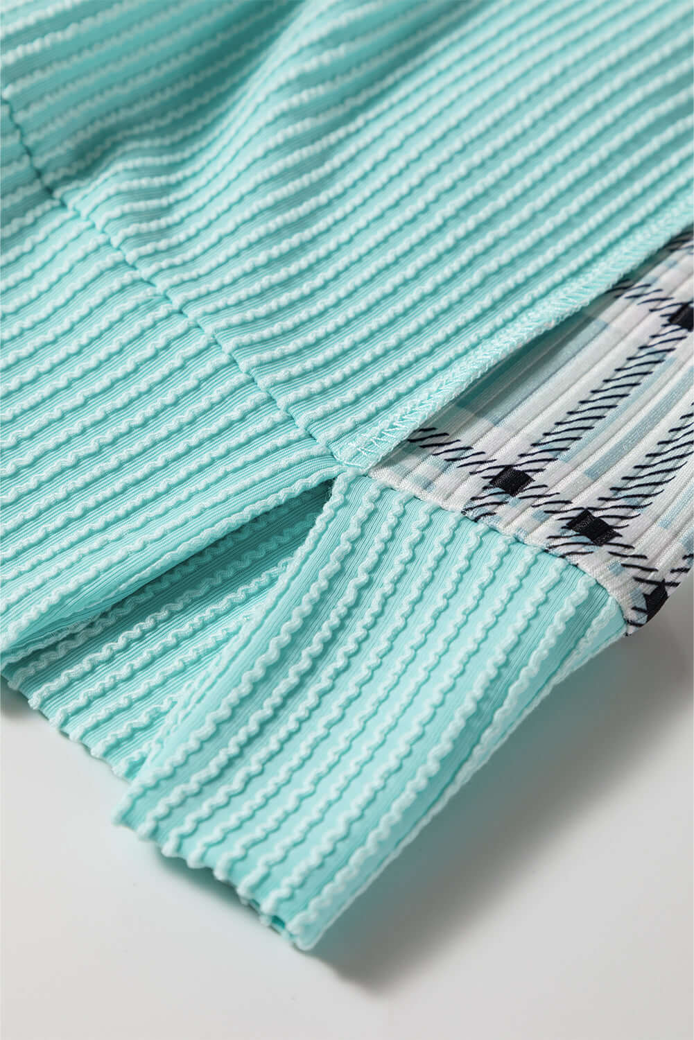 AQUA AVENUE TOP close-up, showcasing ribbed texture and plaid patchwork design details.