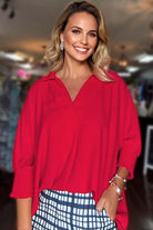 Model wearing a vibrant red TRUE PASSION TOP with a collared V-neck and 3/4 shirred sleeves, styled for chic comfort.