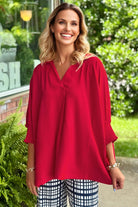 Smiling model wearing a TRUE PASSION TOP in fiery red with V-neck and 3/4 sleeves, showcasing stylish comfort.