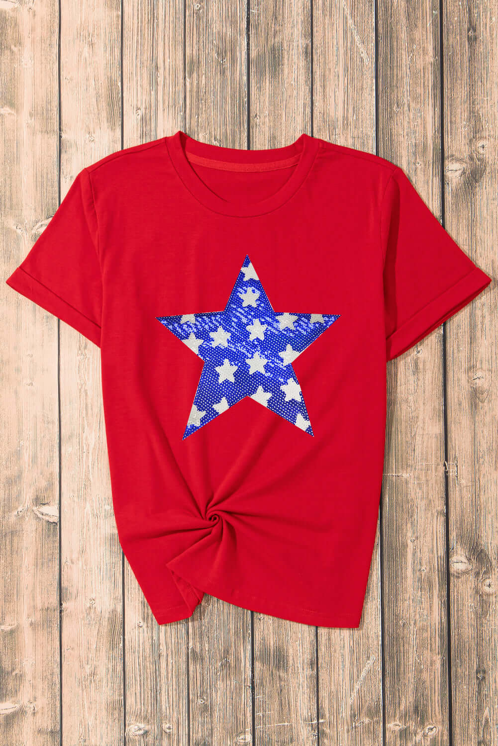 Red crewneck t-shirt with blue sequin star graphic on wooden background.