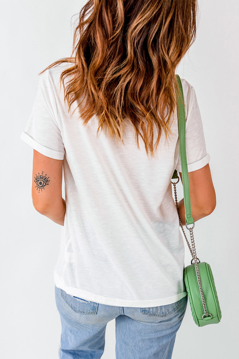 Back view of a woman wearing a white t-shirt with cuffed sleeves and a green bag, showcasing a stylish casual look.