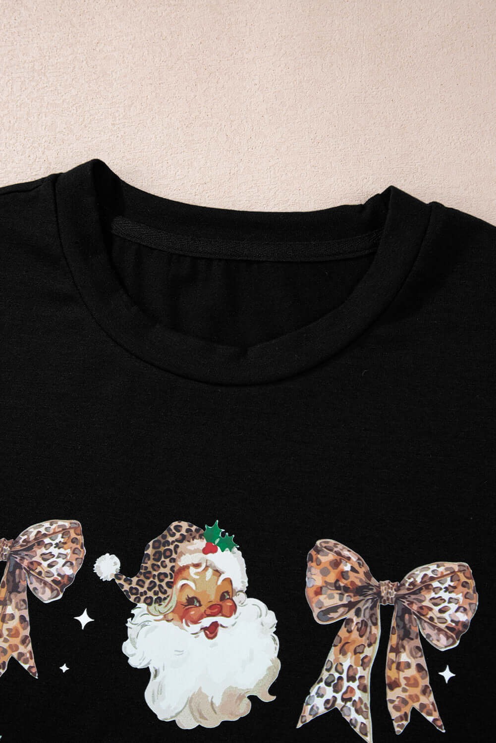 Close-up of festive HO HO HO and Bows T-shirt featuring leopard print, Santa graphics, and bows on a black background.