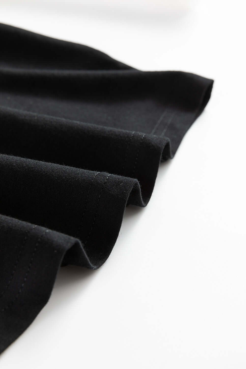 Close-up of a smooth, black fabric showcasing the elegant drape and stitch detailing of a T-shirt.