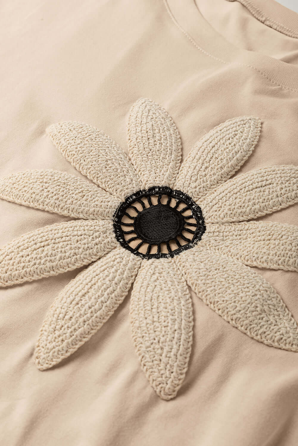 Crochet floral graphic of a daisy on a beige tee, showcasing bohemian style and relaxed design.