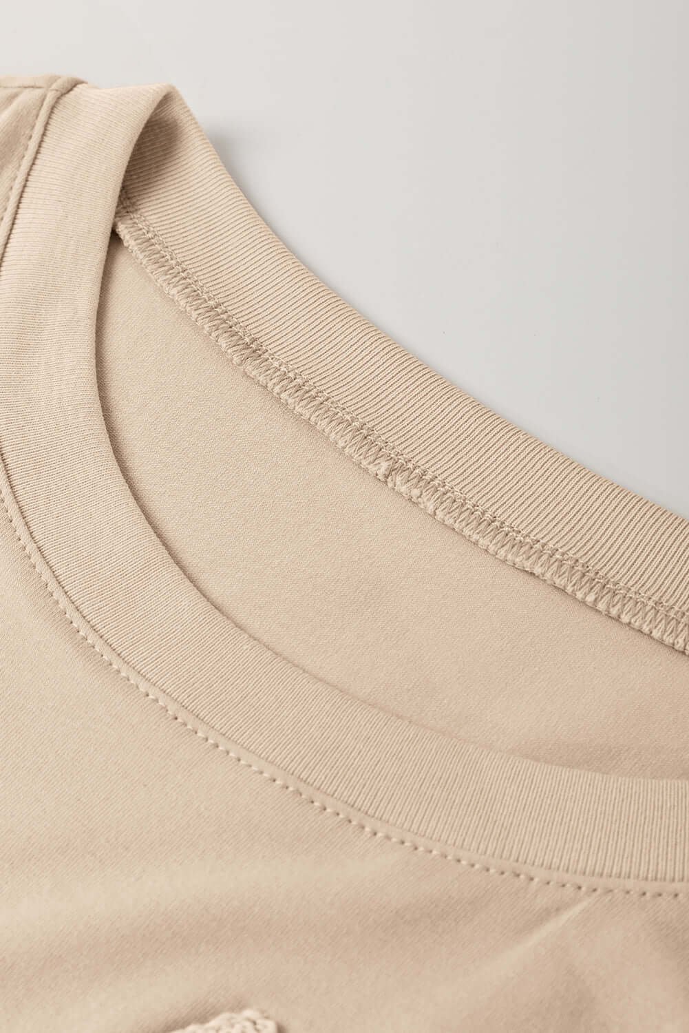 Close-up of the neckline of the Morning Daisy crochet floral graphic tee in a soft beige color.