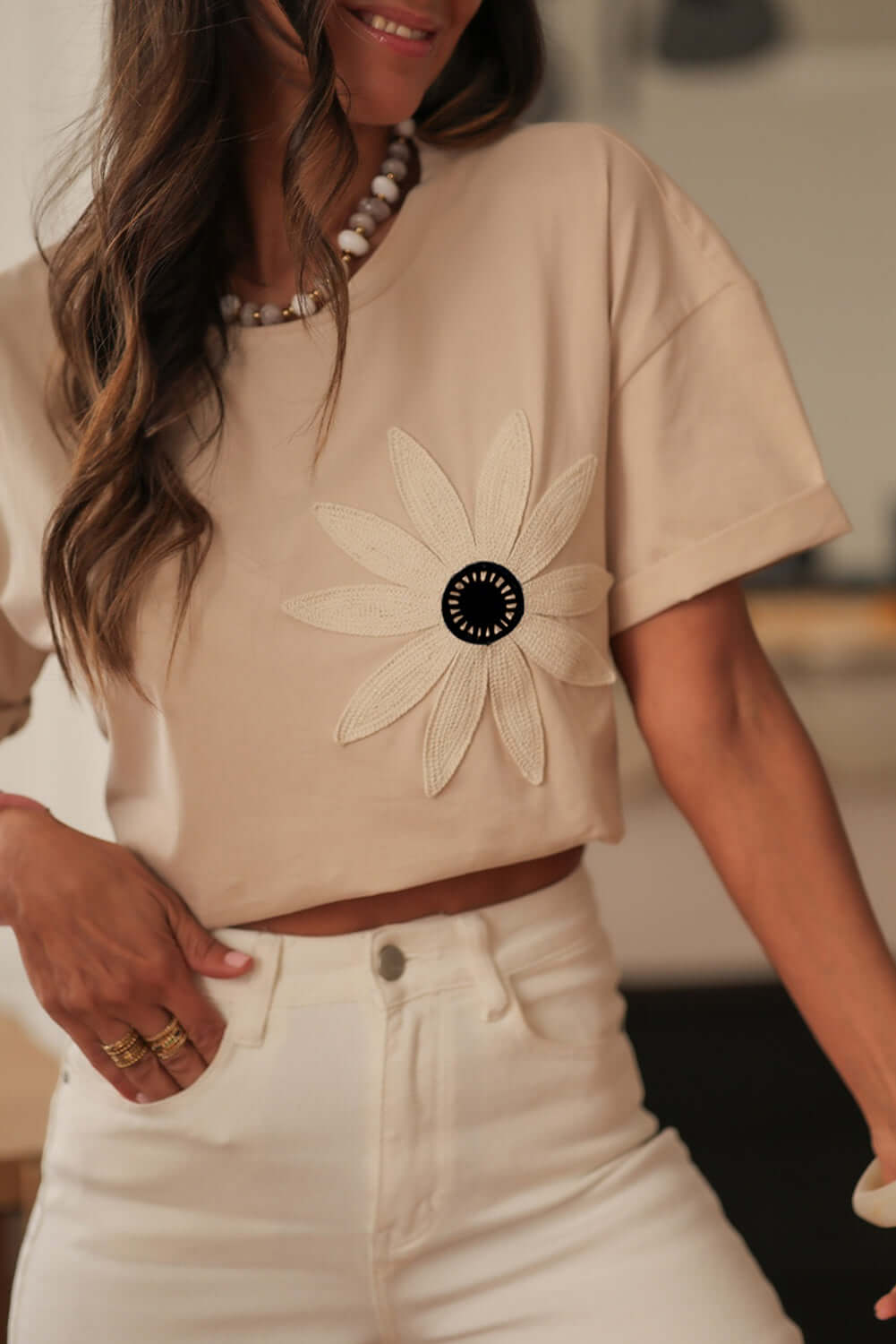 Woman wearing a cream crochet floral graphic tee with drop shoulders and high-waisted white jeans.