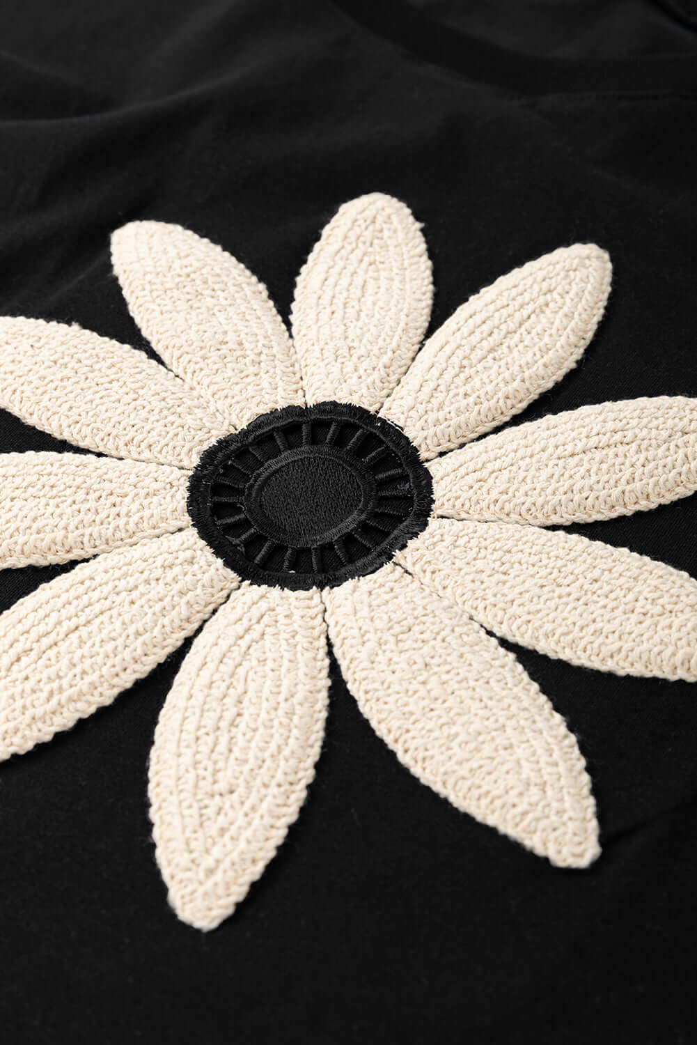 Close-up of crochet floral graphic featuring a large daisy design on a black tee, perfect for a bohemian style.