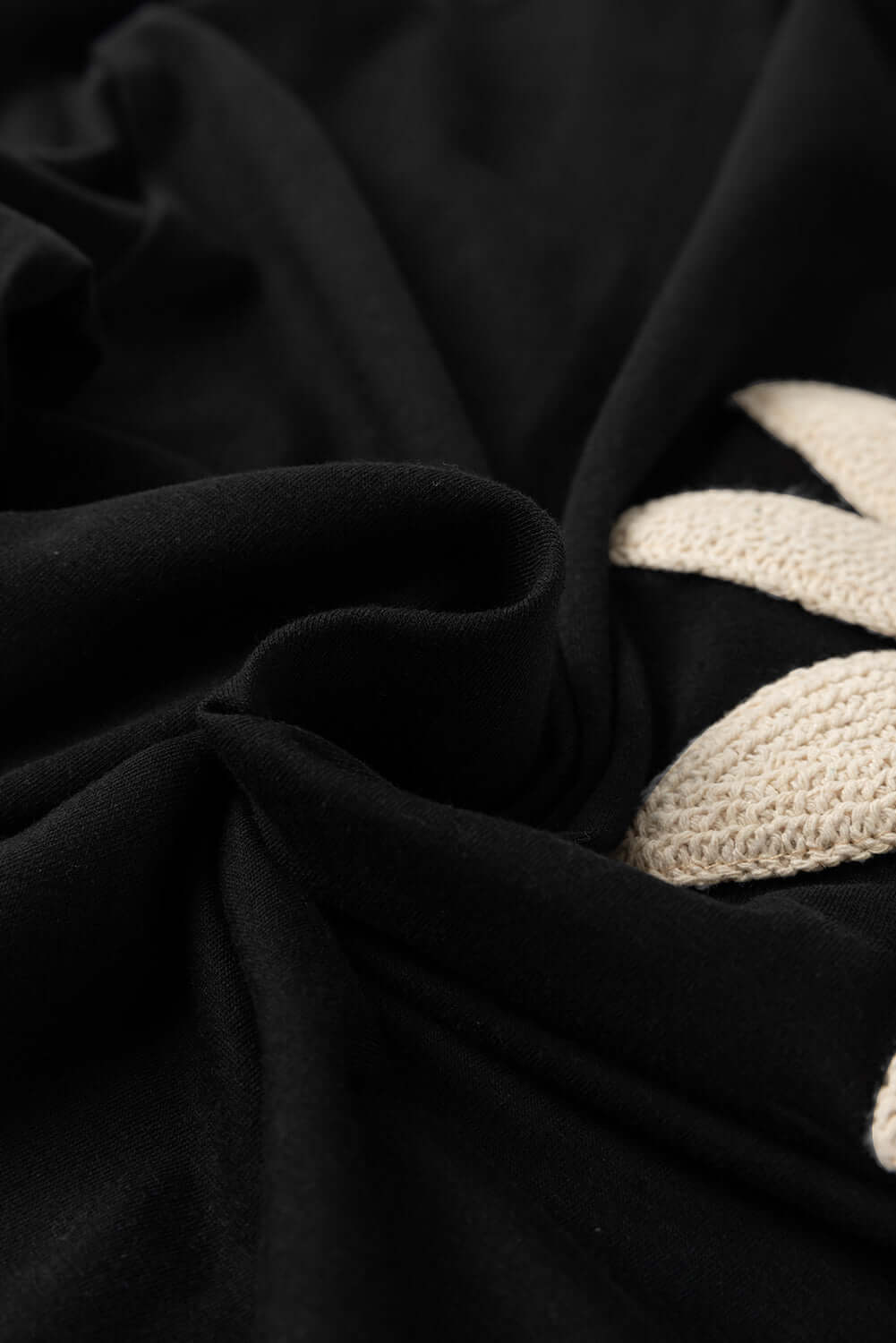 Close-up of black fabric featuring a crochet floral design, showcasing soft texture and intricate details.