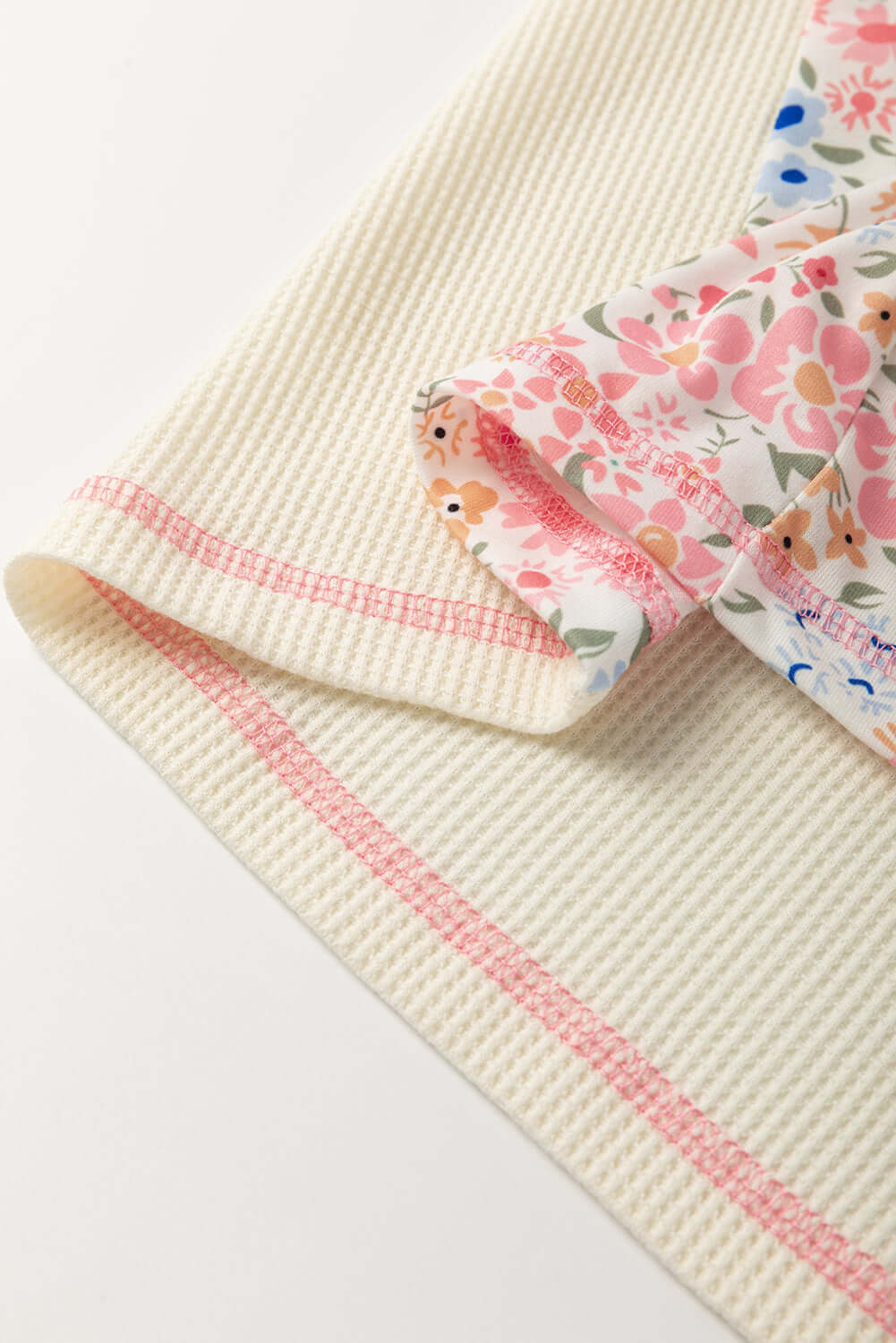 Close-up of the beige waffle knit top with floral sleeves and pink stitching details.