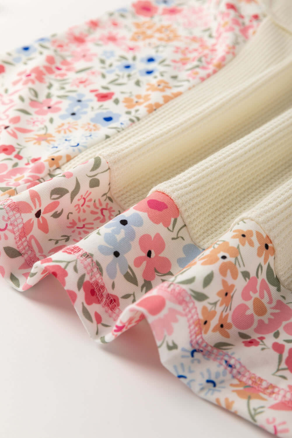 Close-up of beige waffle knit top with floral accents, showcasing soft texture and vibrant colors.
