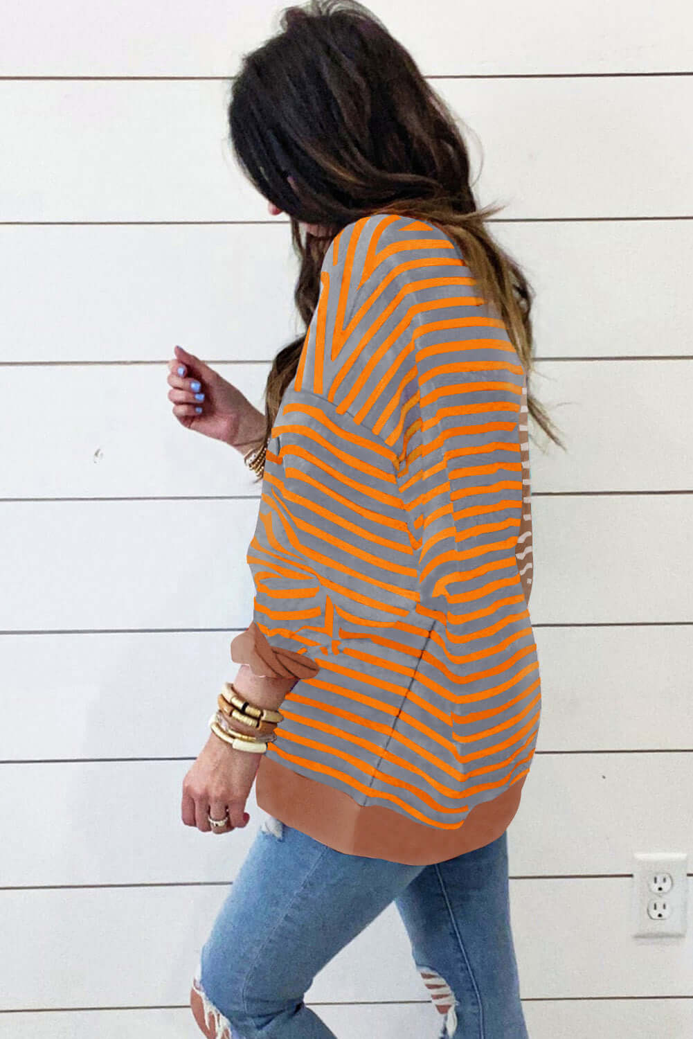 A woman wearing a MAPLE CIDER CREWNECK TOP in a brown and orange stripe colorblock design, styled with relaxed jeans.