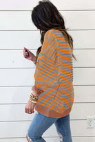 A woman wearing a MAPLE CIDER CREWNECK TOP in a brown and orange stripe colorblock design, styled with relaxed jeans.