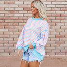 Model wearing the SALTWATER TAFFY TOP with pink and aqua stripes, styled with denim shorts against a brick wall.