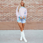 Model wearing SALTWATER TAFFY TOP with pink and aqua stripes, paired with shorts and white boots, against a brick wall.