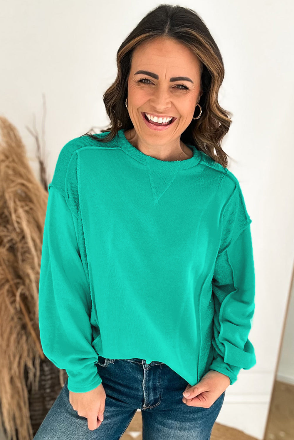 Woman smiling in a teal We Meet Again crewneck sweatshirt, showcasing its relaxed fit and stylish design.