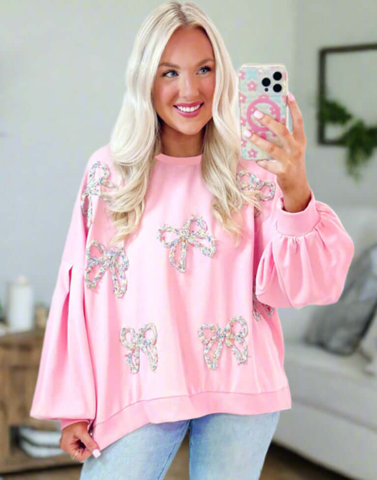 A stylish model wearing THE BOWTIQUE Top (pink) with embroidered bows and lantern sleeves.