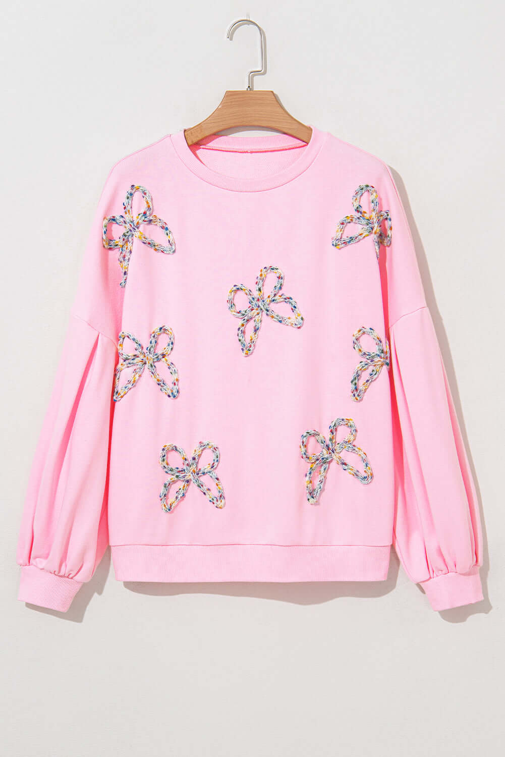 THE BOWTIQUE Top (pink) with embroidered bows and lantern sleeves on a hanger.