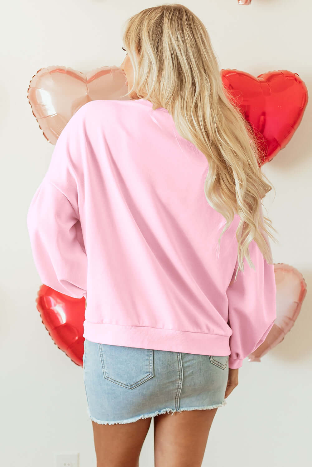 Back view of THE BOWTIQUE Top (pink) with lantern sleeves, styled with a denim skirt and heart balloons.