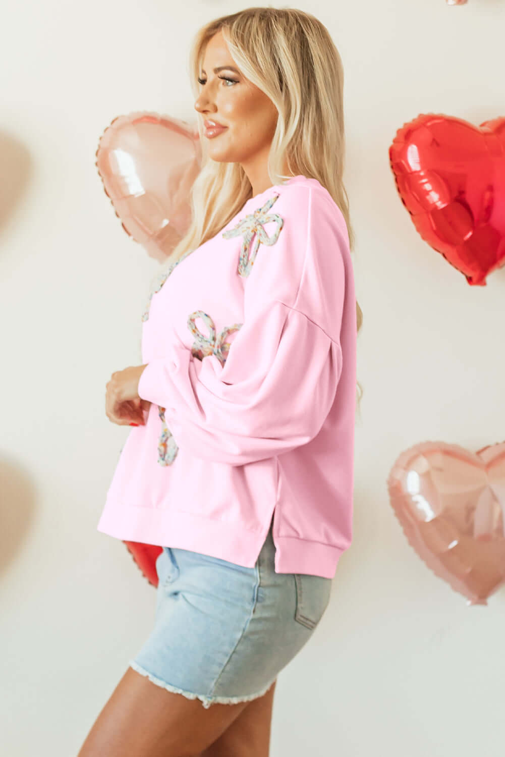 THE BOWTIQUE Top (pink) worn by a model, featuring embroidered bows and lantern sleeves, perfect for a chic look.