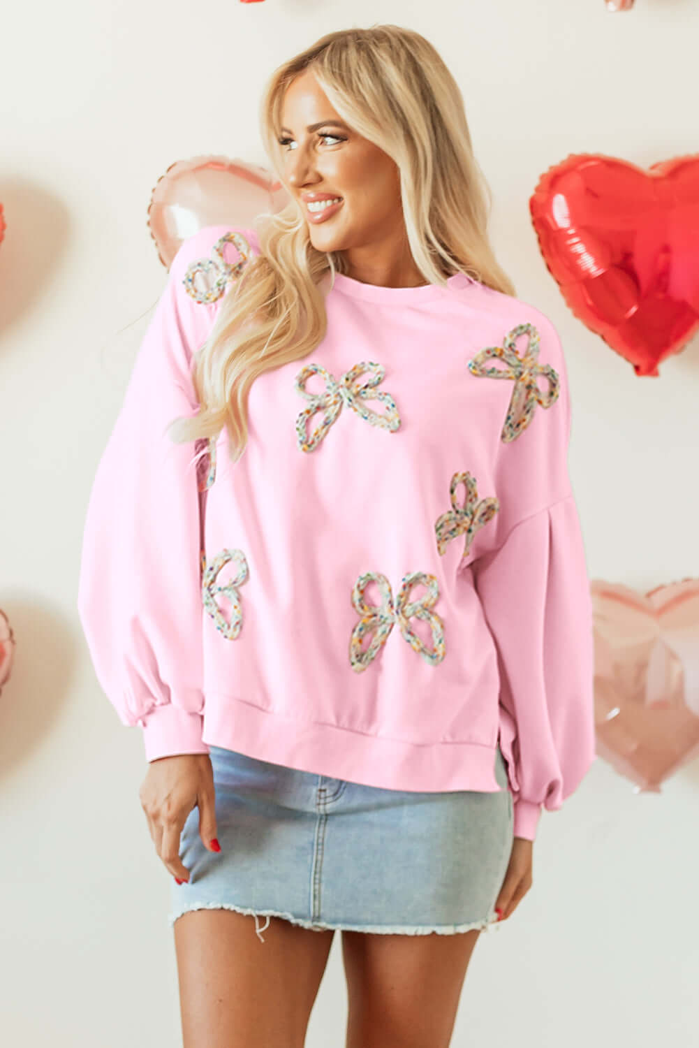 Model wearing THE BOWTIQUE Top (pink) with embroidered bows and lantern sleeves, paired with a denim skirt.