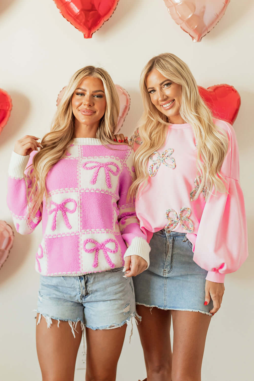 Two models wearing THE BOWTIQUE Top (pink) and another pink pullover, surrounded by heart balloons.