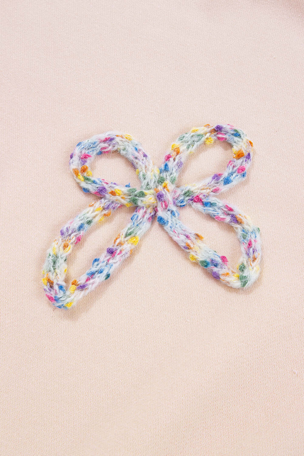 Close-up of colorful embroidered bow detail on The Bowtique Top, enhancing its chic beige pullover design.