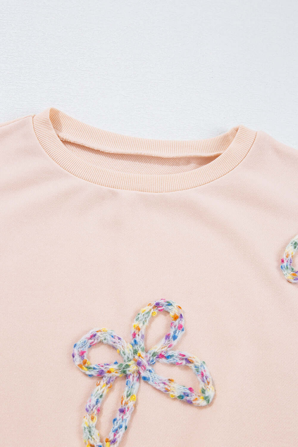 Close-up of The Bowtique Top in beige featuring colorful embroidered bows on a soft fabric.