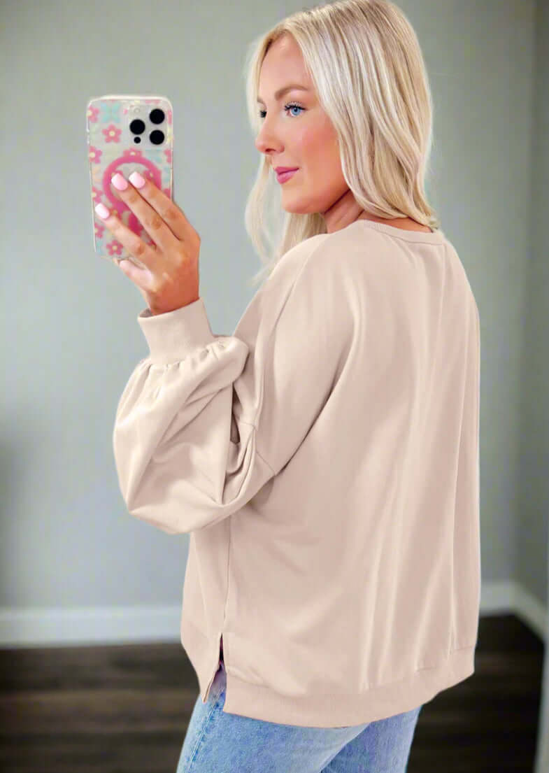 The Bowtique Top in beige with embroidered bows and lantern sleeves, paired with jeans for a chic look.