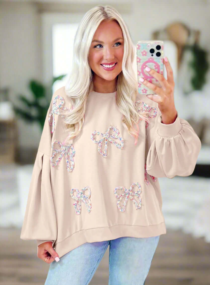 Model wearing The Bowtique Top, a beige pullover with embroidered bows and lantern sleeves, perfect for casual outfits.