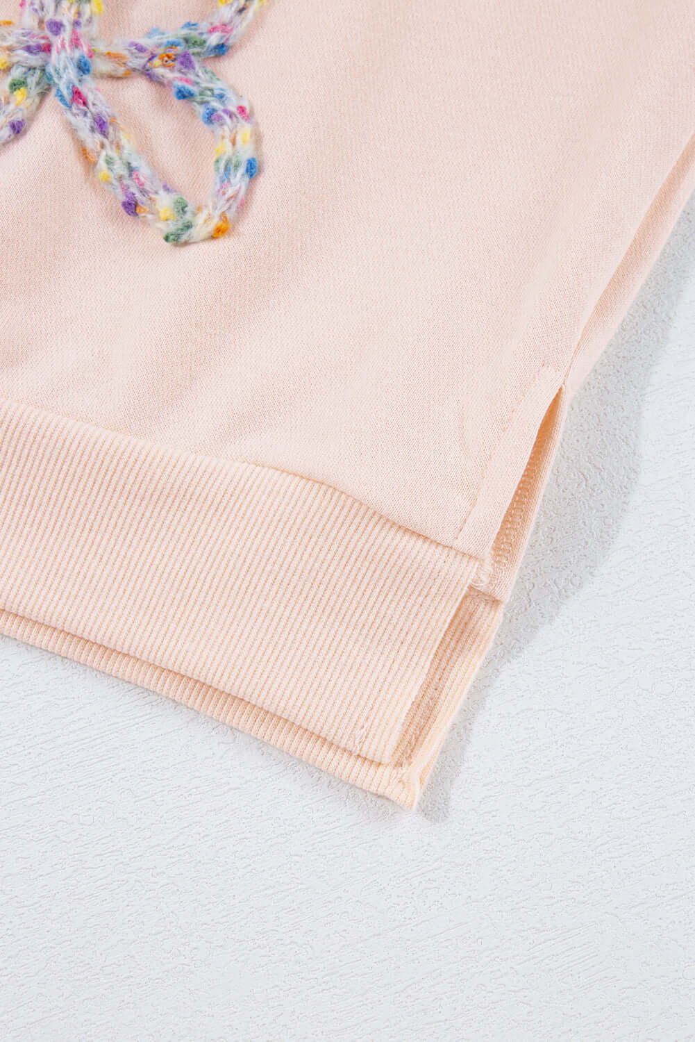 Close-up of The Bowtique Top in beige, featuring colorful embroidered bows and ribbed hem detail.