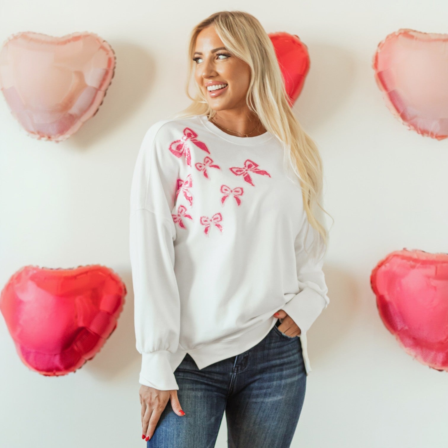 DARLING DETAILS TOP featuring a woman in a white oversized sweatshirt with pink bow details, surrounded by heart-shaped balloons.
