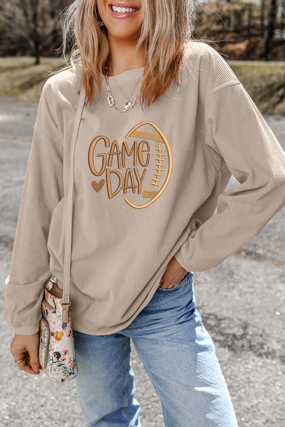 Model wearing LOVE OF THE GAME CORDED CREW in Harvest Beige, featuring 'Game Day' embroidery and a relaxed fit.