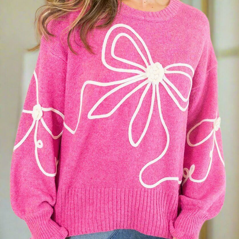 Model wearing TRIP TO REMEMBER Sweater with corded bow accents, relaxed fit, and ruffled cuffs in pink.