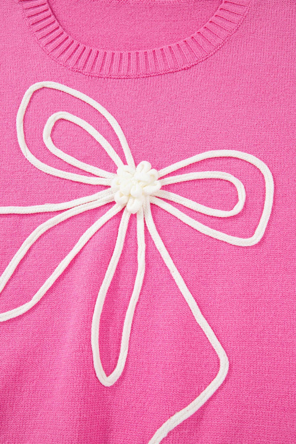 Close-up of soft pink sweater with corded bows and white ruffled cuff details for a trendy look.