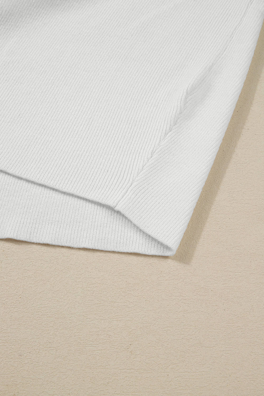 Detail of the MOUNTAIN AIR SWEATER in cream color, showcasing the ribbed knit texture on a beige background.